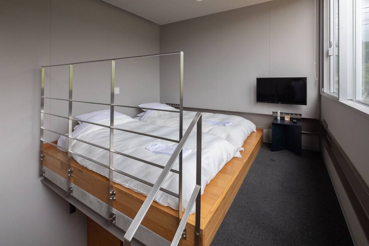 Uma cama beliche com televisão e escrivaninha num quarto com janela.
