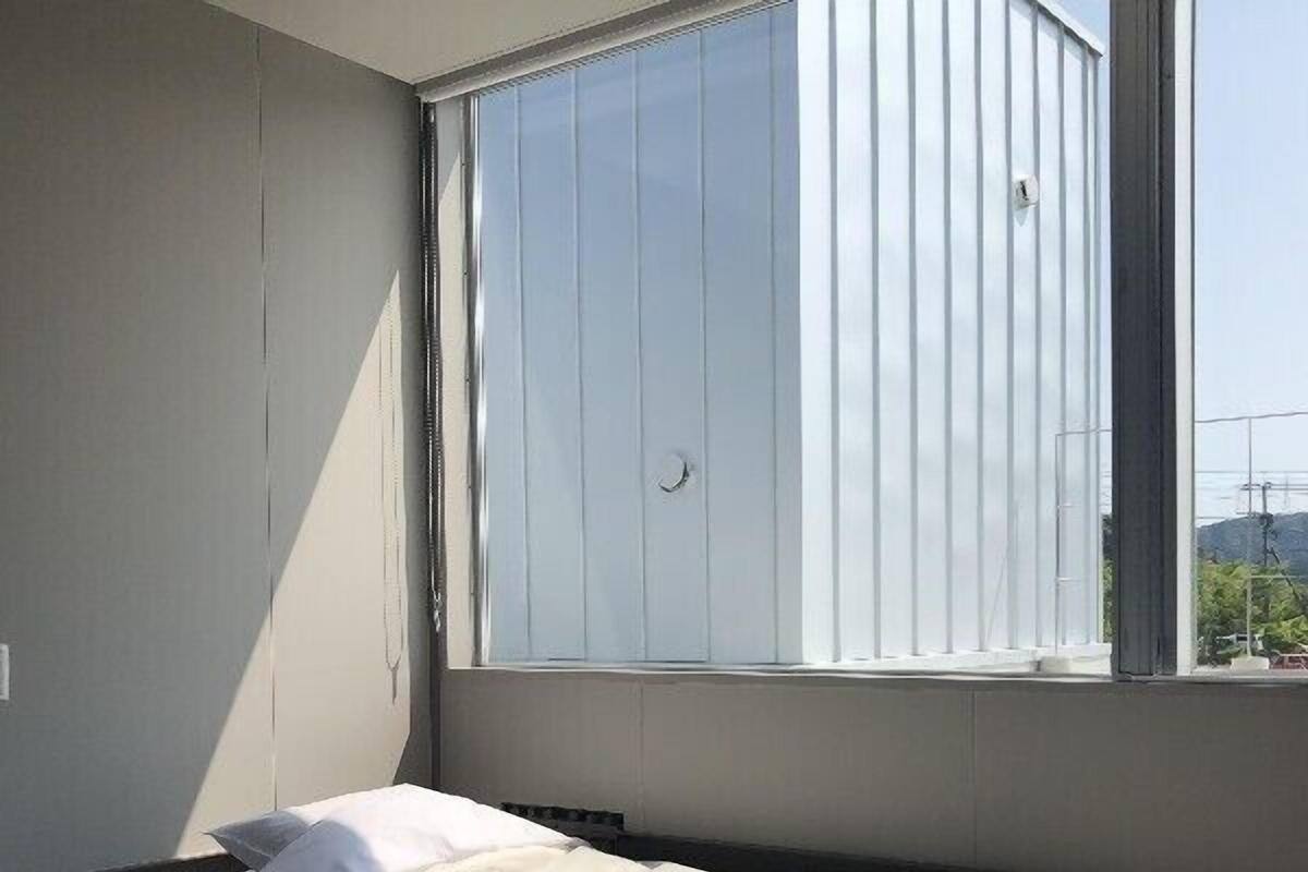 Quarto com uma cama, janela com persianas e vista para o exterior.
