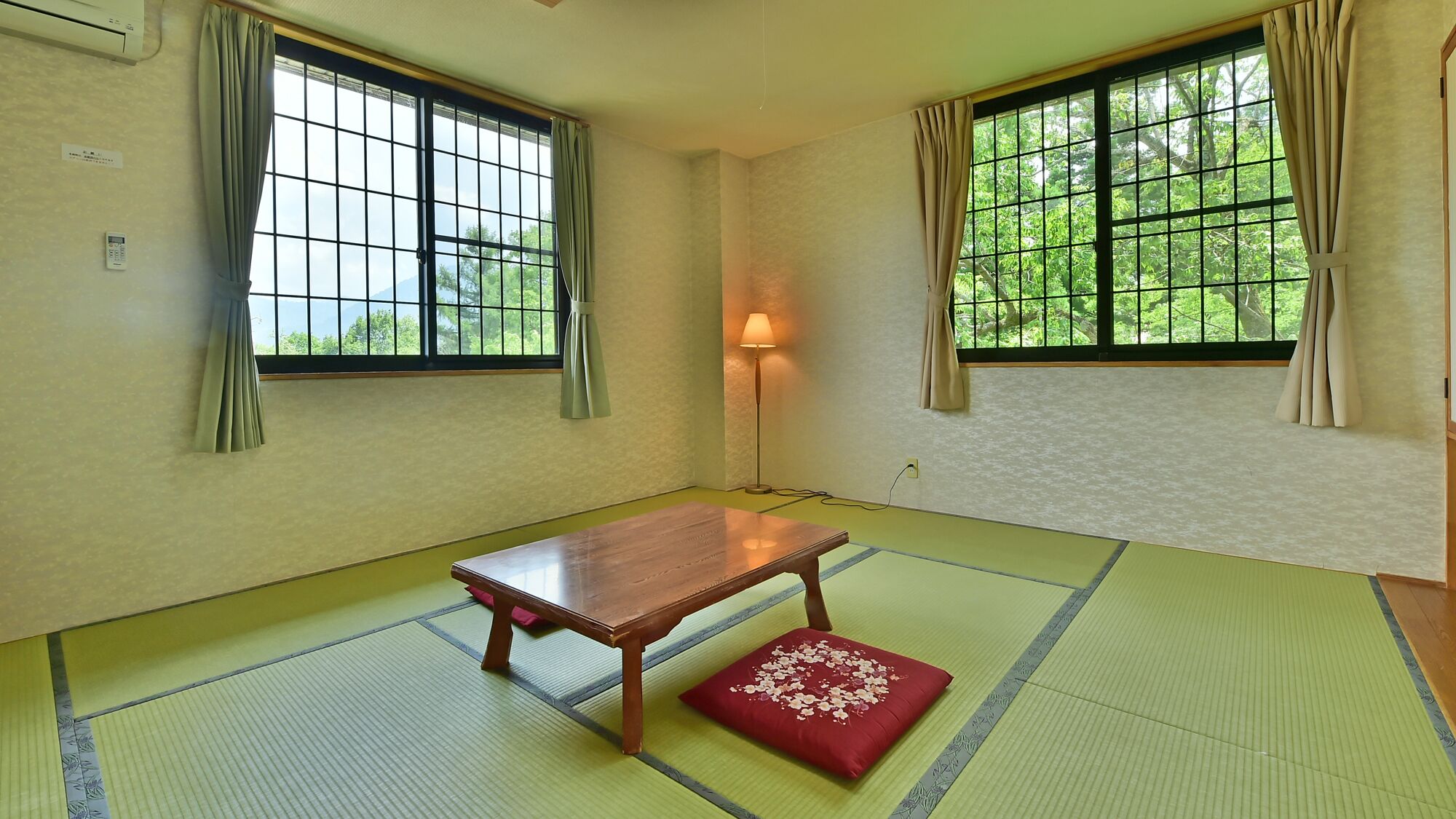 A room with tatami mats, a wooden table, a red cushion, and a lamp.