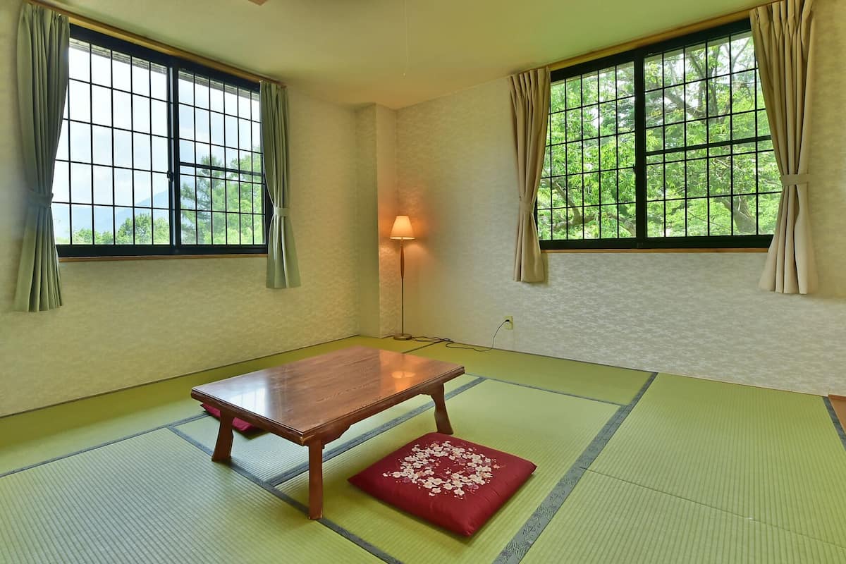 Ein Zimmer mit Tatami-Matten, einem Holztisch, einem roten Kissen und einer Lampe.