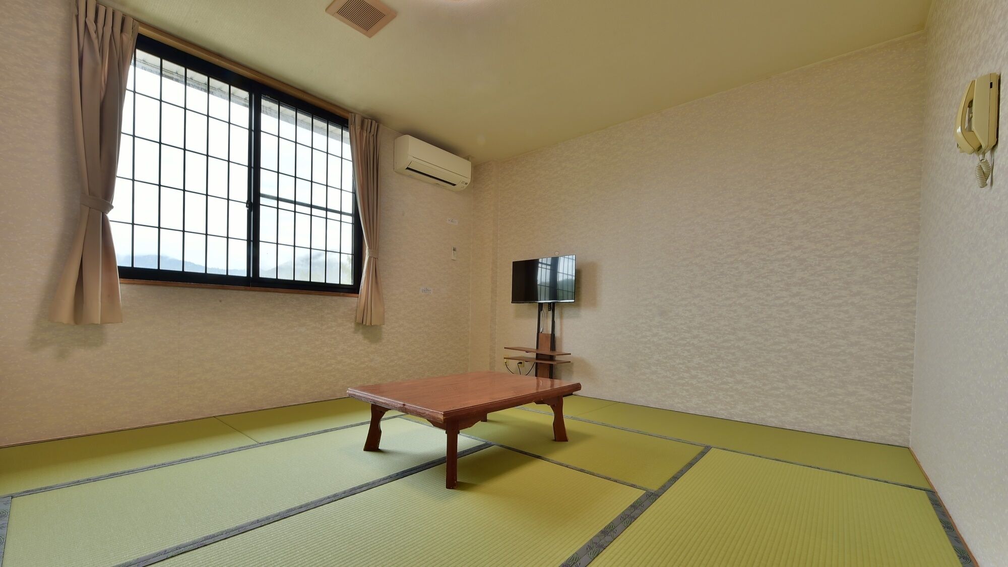 A room with tatami flooring, a wooden bench, a television, and a window with curtains.