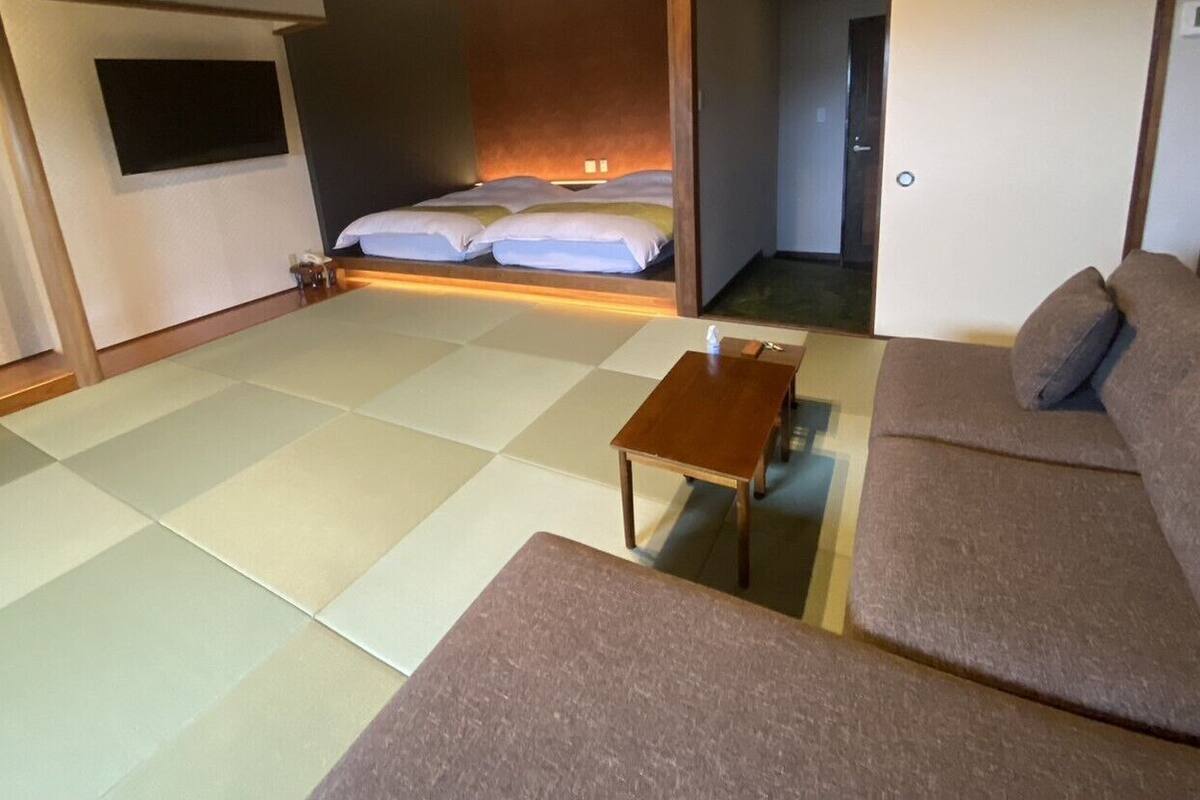 Quarto com tatame, um sofá, uma pequena mesa de madeira e uma cama com almofadas.