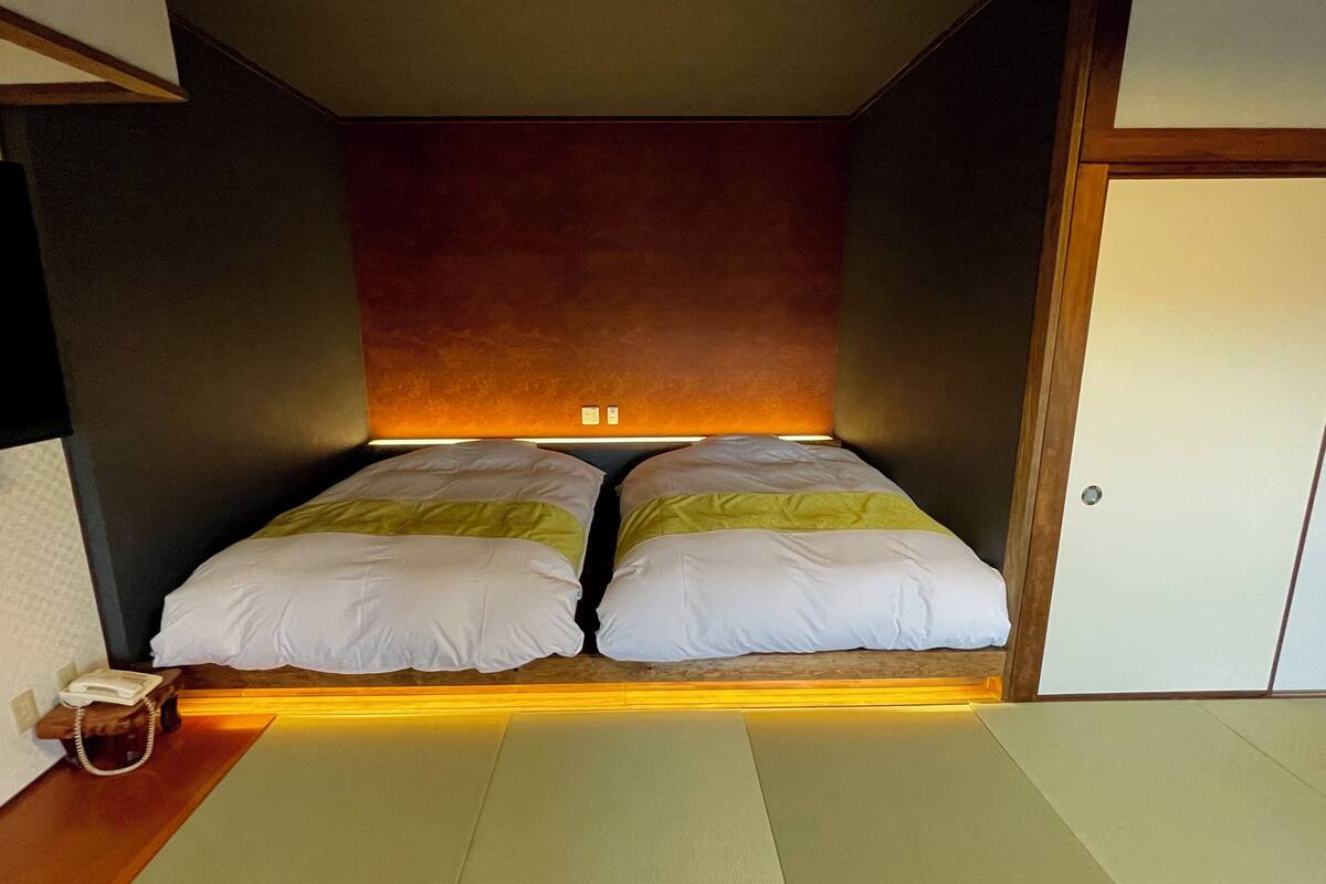 Quarto com cama, telefone ao lado e chão de madeira.