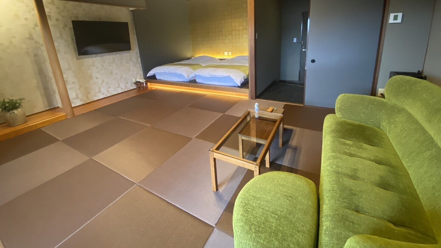 A room with tatami flooring, a bed with white bedding, a green sofa, and a small wooden table.