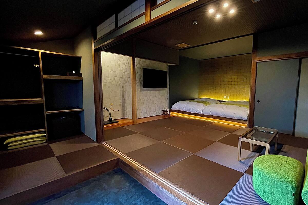 Quarto de hotel moderno com cama, mesa pequena, cadeira verde, closet espaçoso e vista para a cidade.