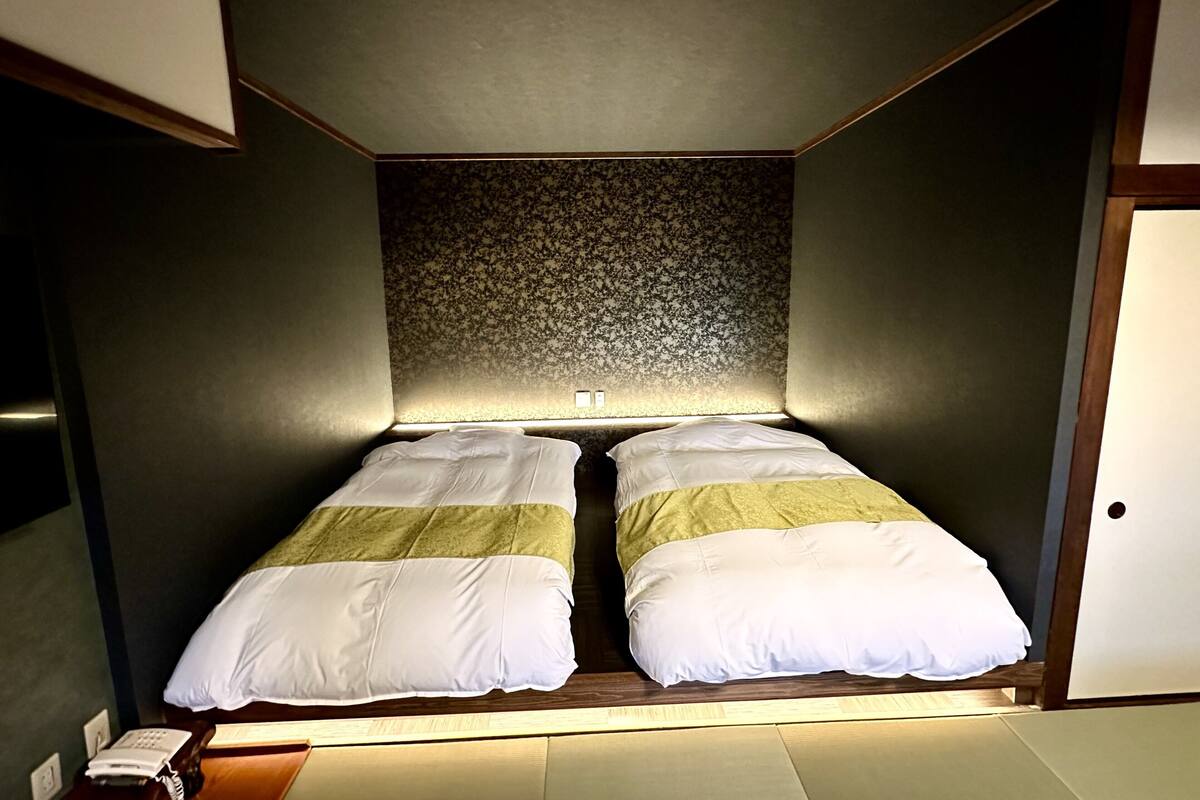 Quarto pequeno e moderno, com uma cama, telefone de apoio e uma porta.