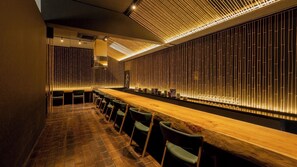 A bar area with a long wooden counter, green bar stools, and a wall with vertical light strips. - Tamana Onsen Nakoikan Villa Tamayura (Tamana)