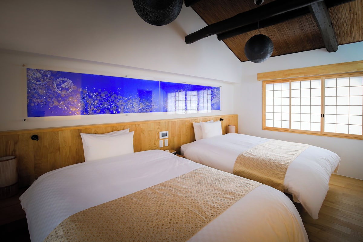 Ein Hotelzimmer mit zwei Betten, einem großen Fenster und einem an der Wand befestigten Aquarium.