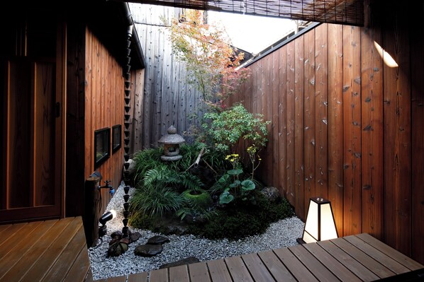 Une clôture en bois, une lanterne en pierre et un petit jardin avec du gravier et des plantes.