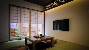 A traditional Japanese room with tatami flooring, a sliding door, a table with a tea set, and a TV mounted on the wall. - Kyo No Yado Gekkoan (Kyoto)