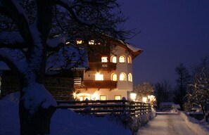 A snow-covered building with multiple windows and a balcony, surrounded by trees and a snow-covered path. - Gasthof Gra Benhof (Vienna)