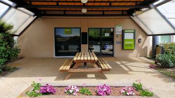A hotel entrance with a wooden bench and flower beds in front.
