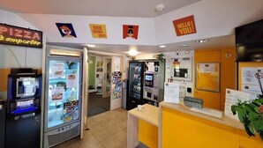 A pizza kiosk with a neon sign, a vending machine, a microwave, and a counter with a menu. - Hotel Lemon (Coudes)
