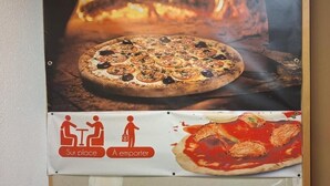 A pizza advertisement with a fire in the background and a sign indicating seating and ordering options. - Hotel Lemon (Coudes)