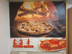 Pizzan mainos, jonka taustalla näkyy tuli ja jossa on kyltti, joka kertoo istumapaikkojen sijainnista ja tilauksen tekemisestä.
