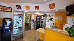 A pizza kiosk with a neon sign, a vending machine, a microwave, and a counter with a menu. - Hotel Lemon (Coudes)