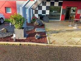Un edificio moderno con fachada a cuadros, mesas al aire libre y un camino de grava.
