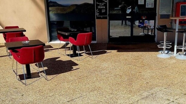 Un espace extérieur aménagé avec des tables et des chaises rouges, un distributeur automatique et une vue sur l’intérieur à travers une porte vitrée.