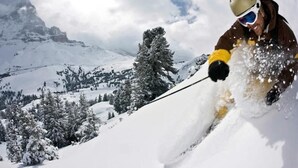 Une personne fait du ski sur une pente enneigée, avec une montagne en arrière-plan.