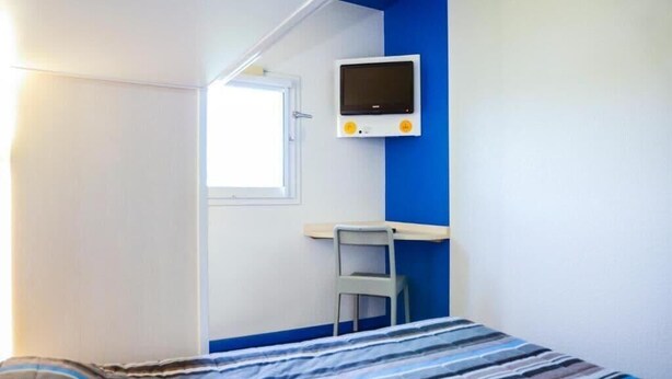 A bedroom with a bed, a desk, a chair, a TV, and a window. - Hotel Lemon (Coudes)