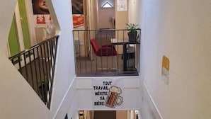 A stairwell with a sign that reads 'TOUT TRAVAIL MERITE SA BIERE' and a red chair in the upper landing. - Hotel Lemon (Coudes)