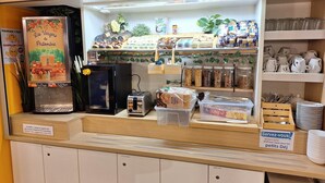 Un comptoir de café avec une machine à café, un grille-pain et divers produits alimentaires. Des panneaux indiquent les prix et un autre panneau signale le service pour les clients.