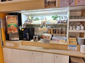 A café counter with a coffee machine, a toaster, and various food items. There are signs indicating prices and a service sign for serving customers. - Hotel Lemon (Coudes)