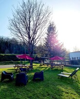 Un área de estar al aire libre con mesas de picnic y sillas, rodeada de árboles y un edificio al fondo.
