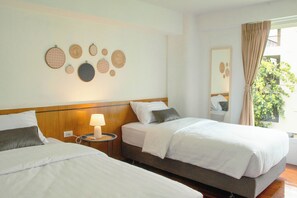 A hotel room with two beds, a bedside table with a lamp, and a wall decorated with circular wall hangings. - Alley & Pier (Bangkok)