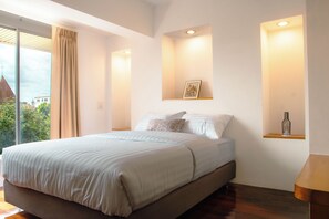 A modern bedroom with a large bed, a view of the outdoors, and a small shelf with a decorative item.