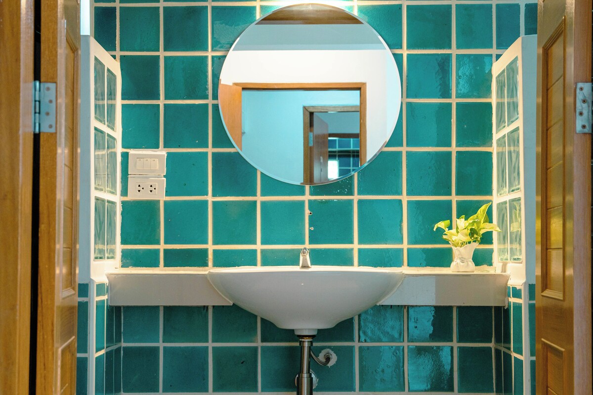 A bathroom with a white sink, a round mirror, and teal tiles.