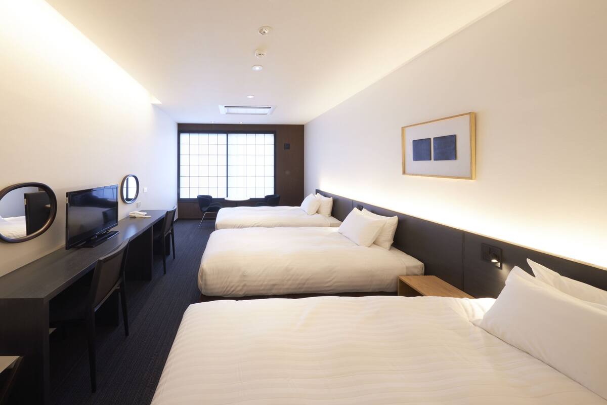 Une chambre d’hôtel avec deux lits, un bureau avec une télévision, un miroir et une fenêtre.