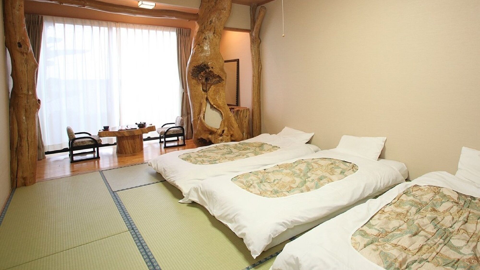A room with two beds, a tatami mat floor, a wooden tree trunk wall, a dining table with chairs, and a large window with curtains.