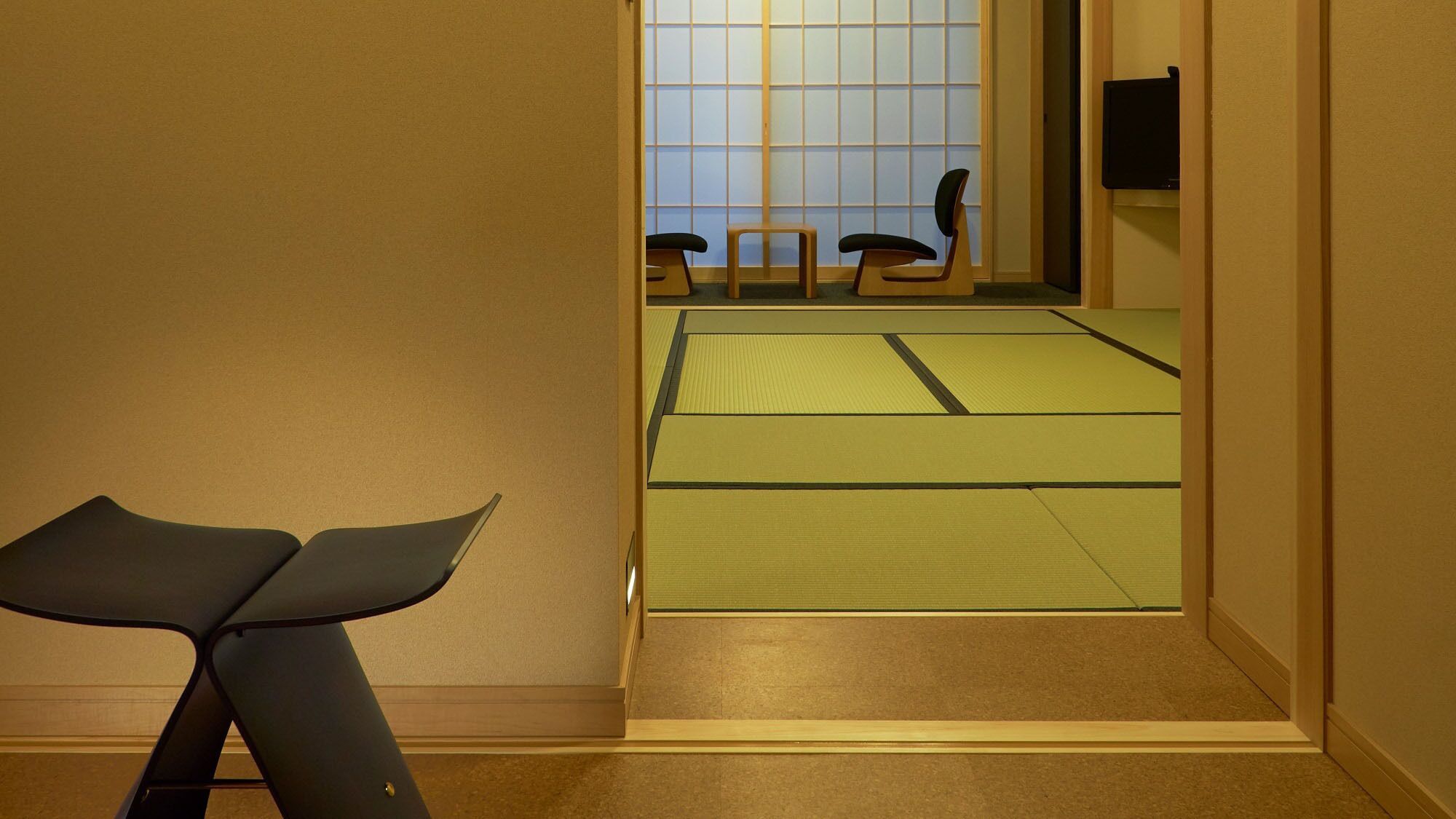 Ein Zimmer mit Tatami-Matten, einem niedrigen Tisch und einer verschiebbaren Tür zu einem anderen Raum.