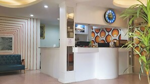 A reception area with a counter, a blue sofa, a decorative wall, and a potted plant. - Happy 2 Hotel Pratunam (Bangkok)