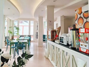 Un hall de hotel con zona de comedor, mostrador de recepción y vistas al exterior.