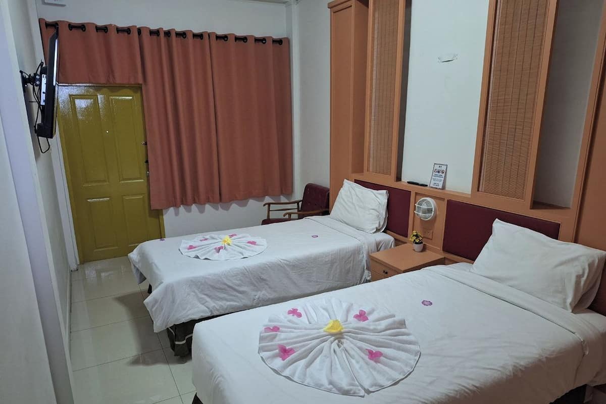 A hotel room with two beds, a wooden headboard, a small bedside table, a nightstand, a TV mounted on the wall, and a door with a curtain.