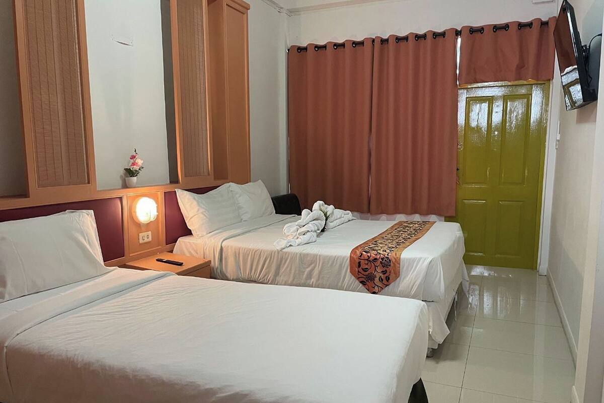 A hotel room with two beds, a nightstand, a lamp, a mirror, and a door.