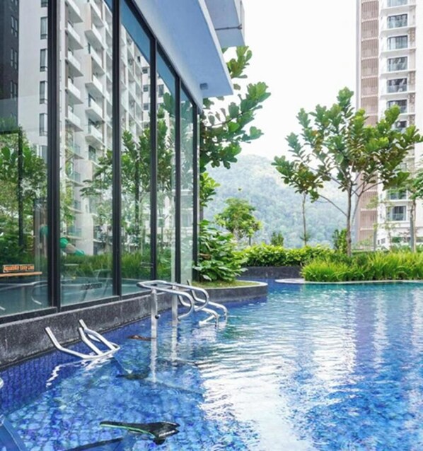 Une piscine dotée d’une paroi en verre, entourée de verdure et de bâtiments modernes.