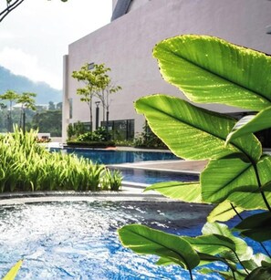 Une piscine avec un bâtiment moderne en arrière-plan et une végétation luxuriante au premier plan.