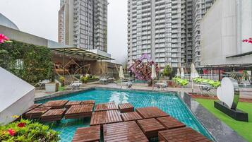 A swimming pool with wooden deck chairs, surrounded by tall residential buildings.