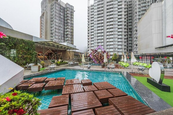 Une piscine entourée de chaises longues en bois, elle-même bordée d’immeubles d’habitation imposants.