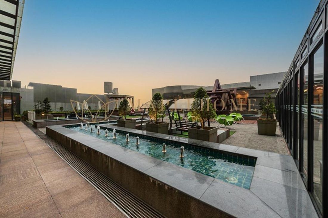A rooftop pool area with a long rectangular pool, surrounded by potted plants and seating areas.