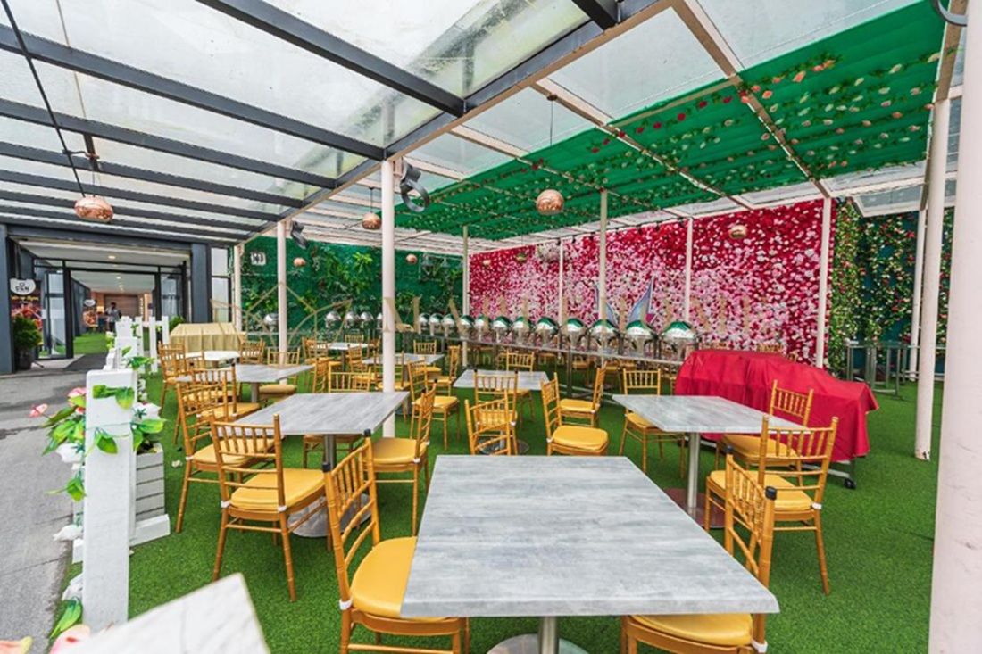 An indoor garden restaurant with tables and chairs, green artificial grass, and a glass ceiling.