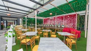 An indoor garden restaurant with tables and chairs, green artificial grass, and a glass ceiling.