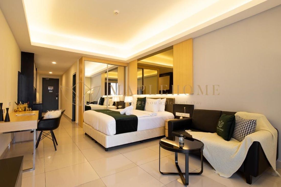 A modern hotel room with a large bed, a sofa, a desk, and a mirror.