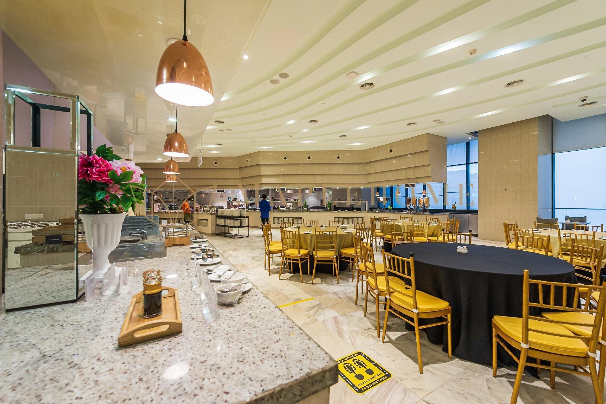 A spacious dining area with round tables and yellow chairs, a marble counter with a vase of flowers, and a modern ceiling design.