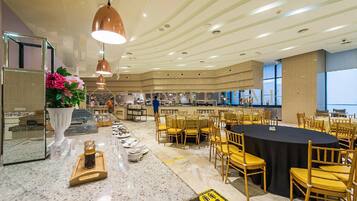 A spacious dining area with round tables and yellow chairs, a marble counter with a vase of flowers, and a modern ceiling design.