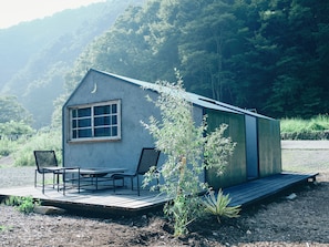 A small cabin with a porch, two chairs, and a table. - Loof Tiny House Camp (Fuefuki)