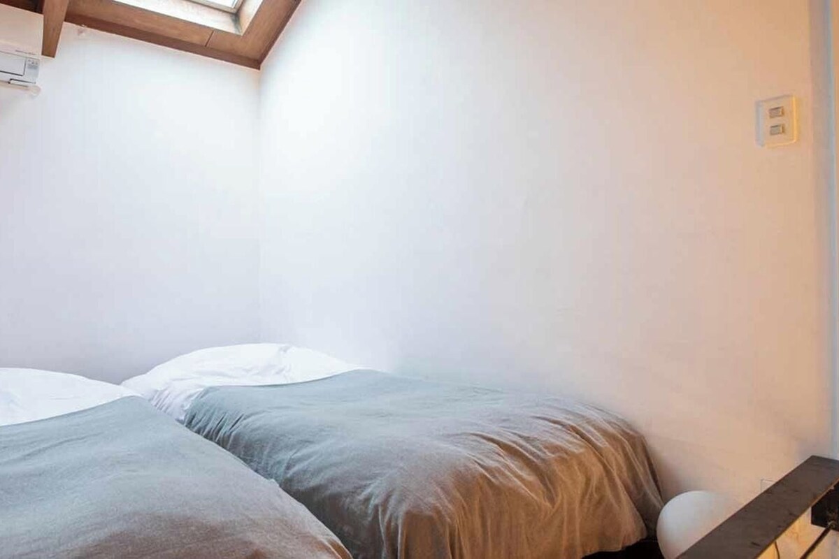Ein kleines Zimmer mit einem Einzelbett, schrägem Dach, Holz-Kopfteil und Wand-Klimaanlage.